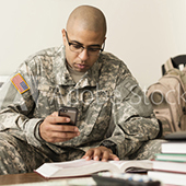 Soldier studing in a book and on a smart phone